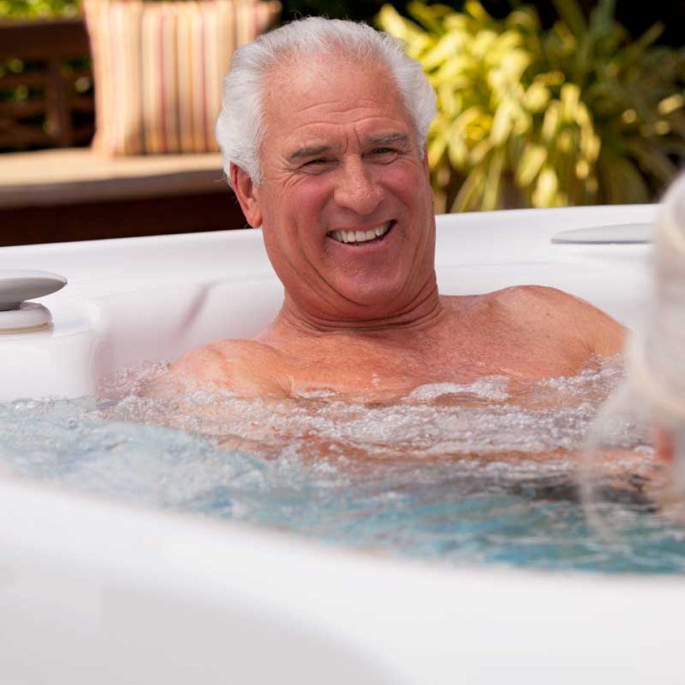 Older gentleman in a hot tub smiling at somebody out of frame